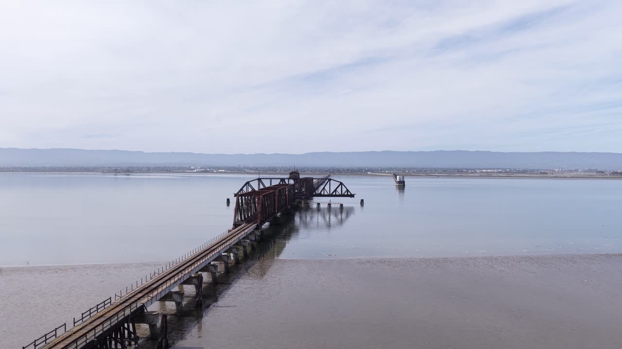 Luftperspektiv af den historiske og forladte Dumbarton Rail Bridge, en svingbro med stålfagværk, der krydser San Francisco-bugten og forbinder Fremont og Menlo Park nær Newark, Californien