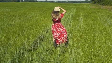 slow motion young girl runs across green field in red dress that flutters in the wind