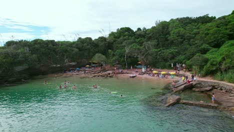 Flyover-dolly-out-of-people-enjoying-Azeda-and-Azedinha-beaches,-Búzios,-Brazil-tourist-boats-in-pristine-waters-with-a-couple-kayaking