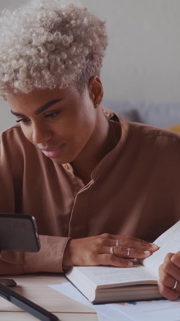 Insegnante afroamericana che legge un libro ad alta voce mentre registra un video su treppiede