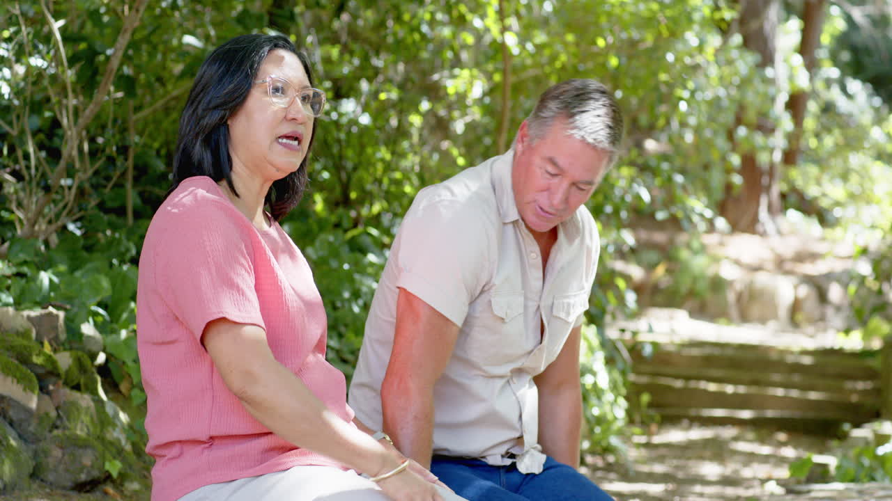 Senior diverse couple sitting on park bench, enjoying conversation and nature together