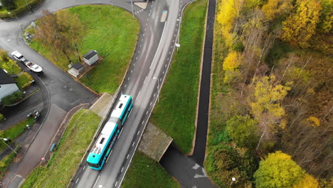 aerial top down shot of driving articulated bus driving on rural road between colorful trees in gothenburg,sweden