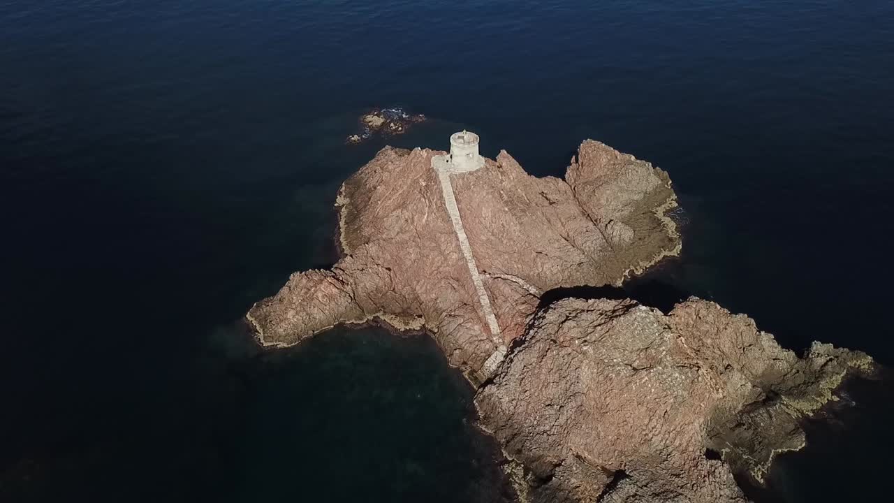 Drone shot approaching a small white limestone island featuring a natural sea cave and rugged cliffs in turquoise Mediterranean waters