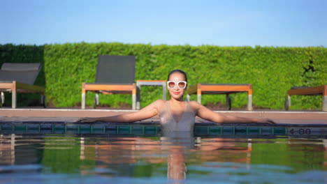 una mujer bonita, joven y en forma en una piscina estira los brazos a lo largo del borde de la piscina