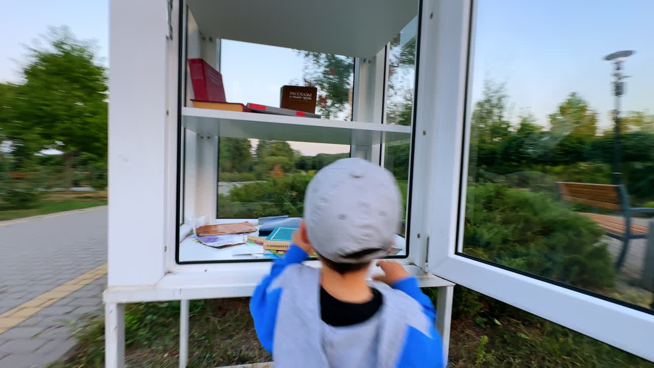 Approaching the toddler walking in the park with his grandpa. Kid takes book from the box.