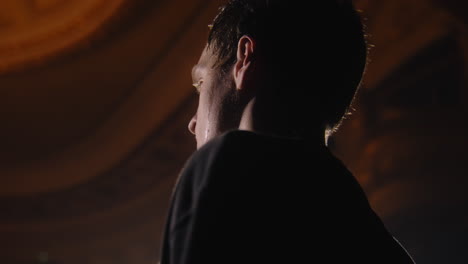 Close up shot of tired ballet male dancer standing on theater stage and training before performance. Sweat flows down his face. Choreography rehearsal. Illuminated theatrical hall. Classical ballet.
