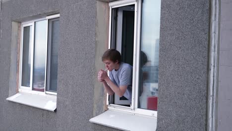 ein mann raucht vor dem fenster eines wohngebäudes