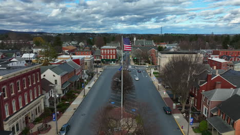 Powerful-cinematic-slow-motion-shot-of-American-flag-waving-in-breeze-in-small-town-America-under-dramatic-daytime-sky-and-clouds