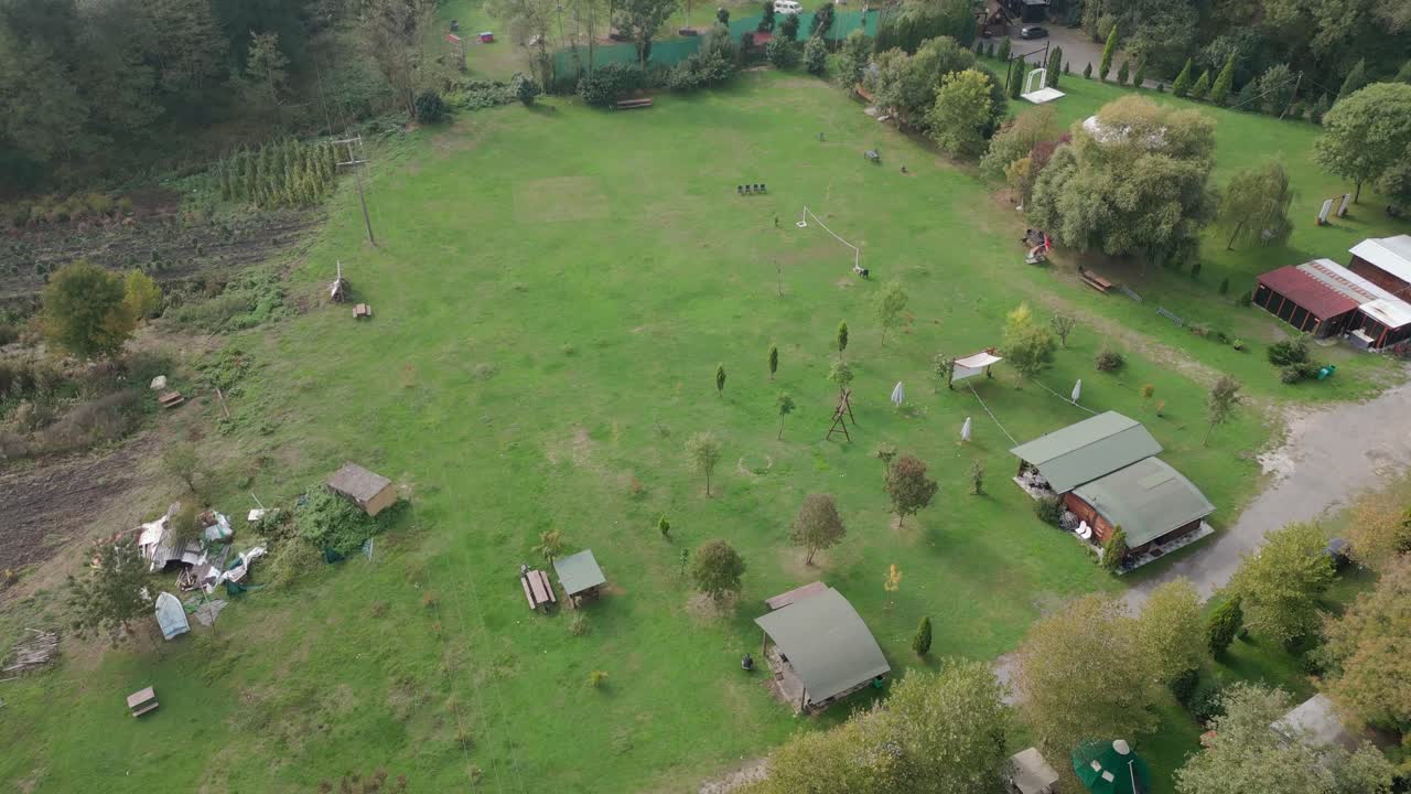 Drone ascending above countryside with scattered houses, fields, and surrounding forest