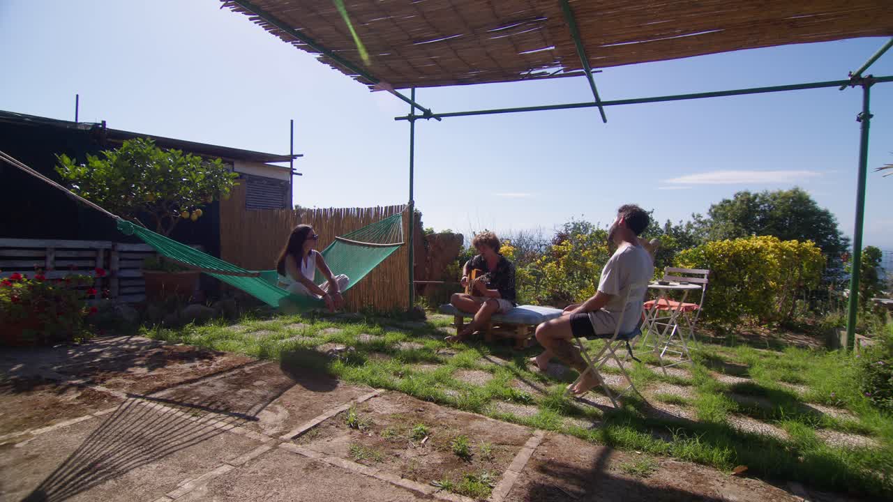 Wide shot of a trio of friends jamming together with an acoustic guitar in a peaceful garden on Capri Island, Anacapri
