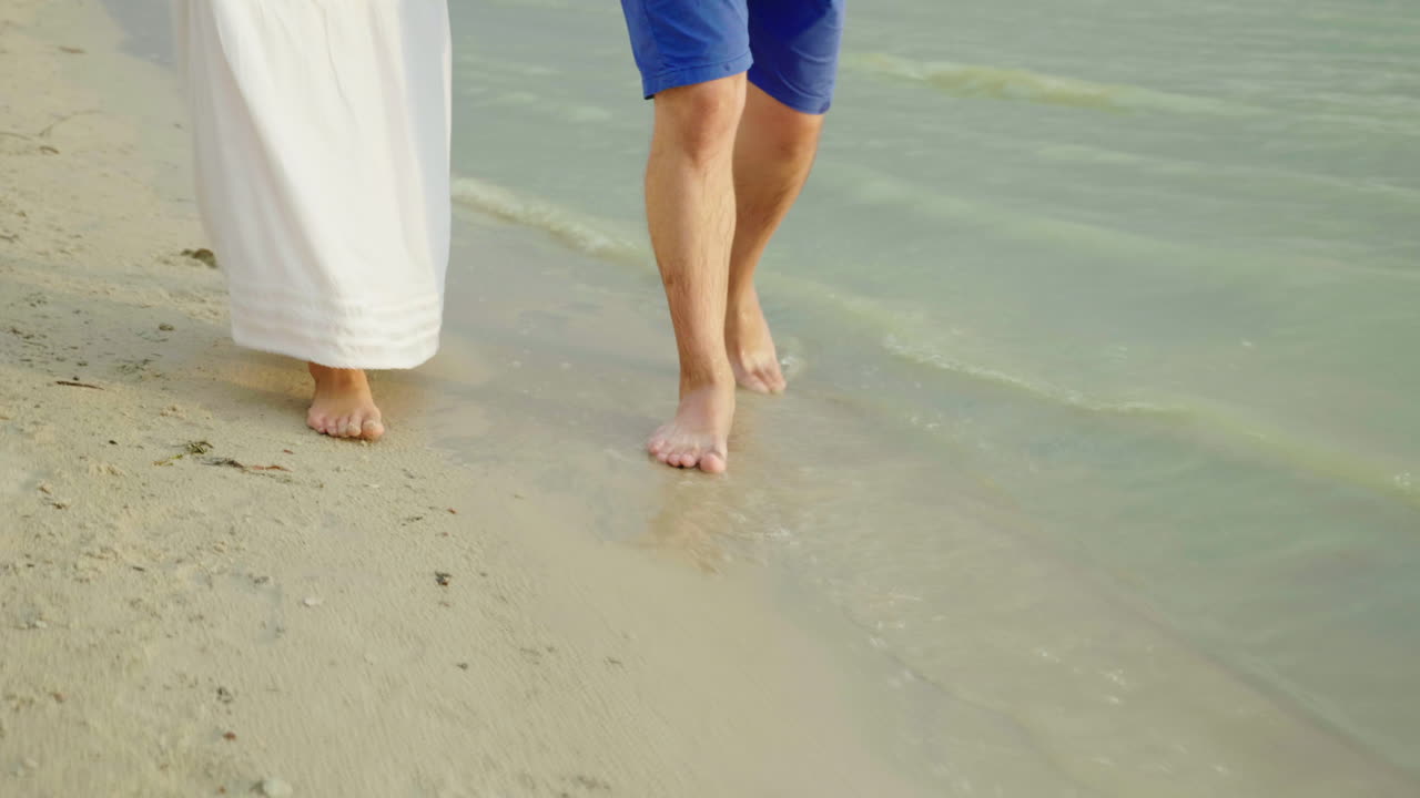 los pies descalzos de un hombre y una mujer caminan juntos por la arena a lo largo del mar de vacaciones en los trópicos 4k