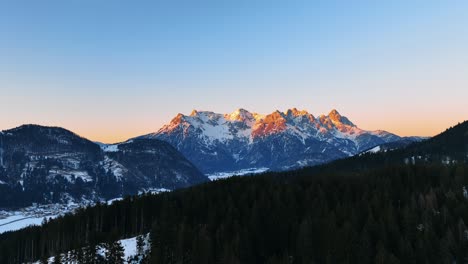 die drohne fliegt über einen berg mit bäumen, der einen großen berg zeigt, der bei sonnenuntergang in österreich von der goldenen sonne beleuchtet wird.