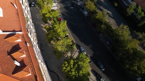 Aerial-view-over-residential-area-with-car-traffic-on-the-road,-red-rooftops-makes-background-from-green-tree-lines-long-the-pedestrian-walking-area