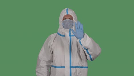 portrait of a man in a protective suit and medical mask looks at the camera waves hello and makes a gesture come here pointing at someone with a finger. green screen, chroma key. slow motion. close up