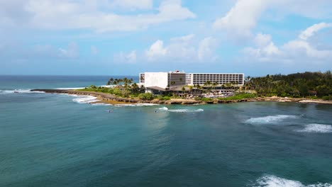 toma cinematográfica de drones de las aguas azules y el edificio en el fondo cerca de la costa de turtle bay, oahu hawai