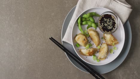 Composition-of-plate-with-gyoza-dumplings-and-soy-sauce-with-chopsticks-on-grey-background