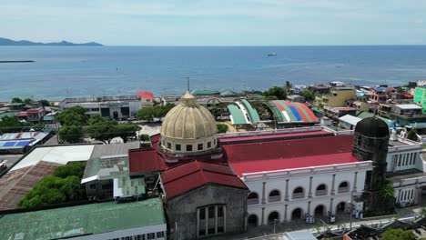 rotating aerial view of old cathedral church in downtown virac, catanduanes with turquoise sea in background