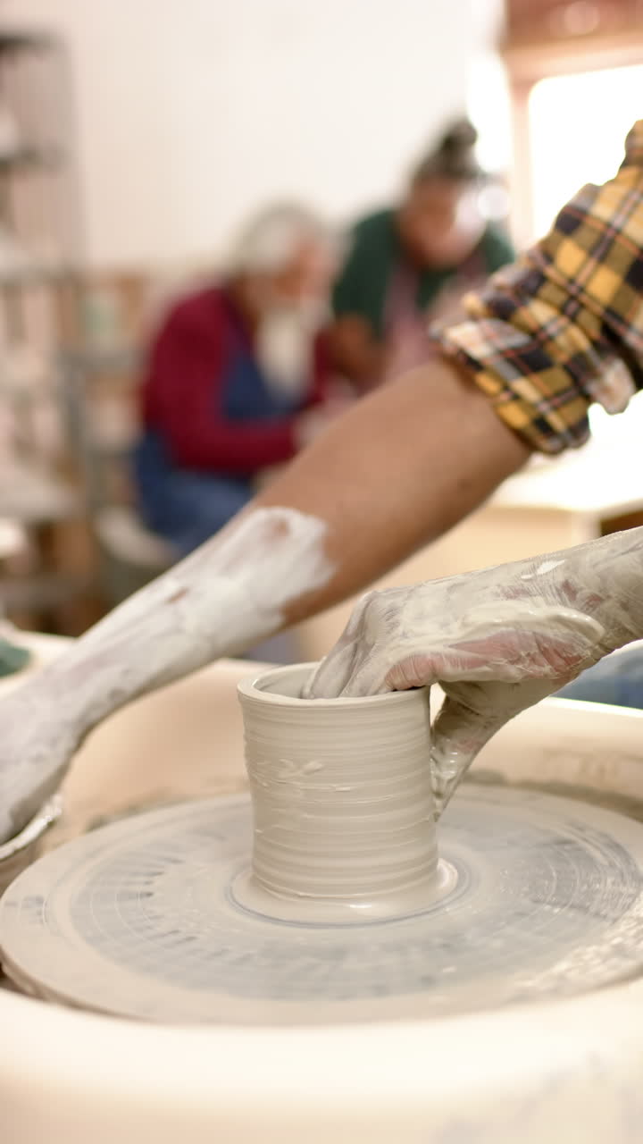 Hands of african american male potter using potter's wheel in pottery studio, slow motion