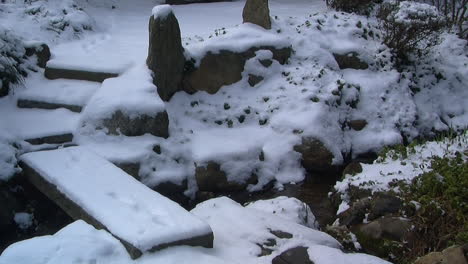 slow zoom-in on snow covered footbridge and japanese garden