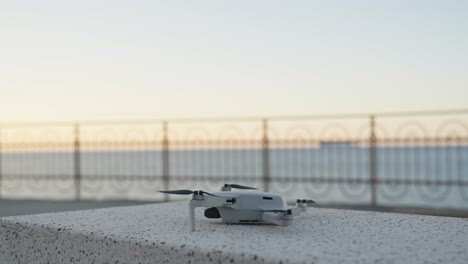 a small drone rests on a stone surface near a seaside railing at sunset