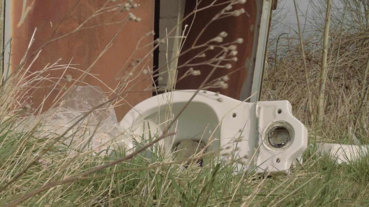 Discarded toilet and rubbish left outside panning shot