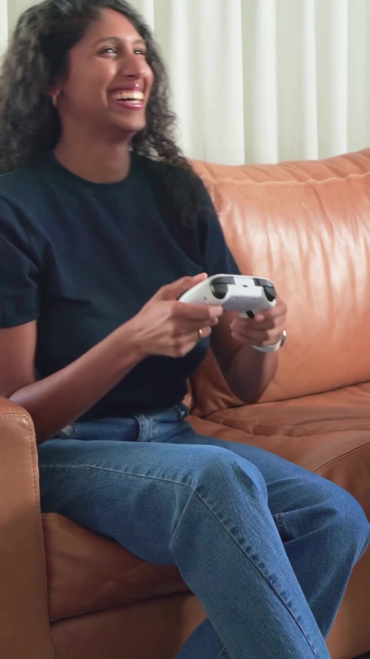 Vertical video: Reaching woman in navy tee taking controller from man on couch for gaming, laughing