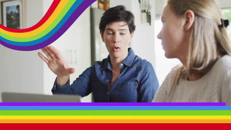 animation of pride rainbow stripes over happy caucasian lesbian couple using laptop and talking