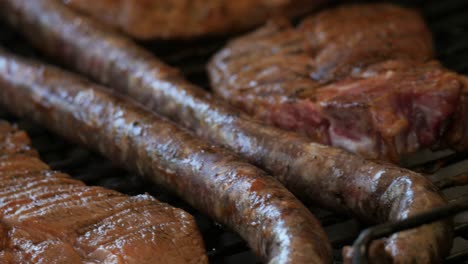 Brutzelnde-Wurst-Und-Schweinefleisch-Auf-Einem-Grill-Aus-Nächster-Nähe-Und-Rutsche