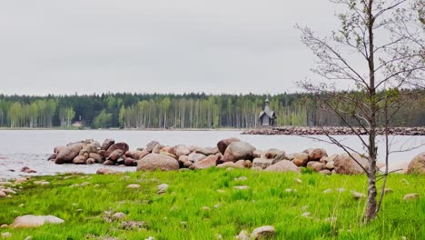 an old chapel stands on a stone promontory on the water in leningrad region russia at cloudy weather, the forest in the background