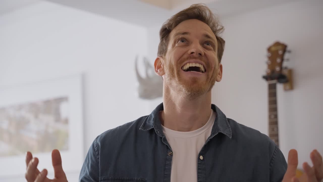 Portrait of happy Cheerful man in a denim shirt speaks energetically to camera, gesturing with his hands in a bright home interior. daylight. explainer, testimonial, webinar, or influencer content