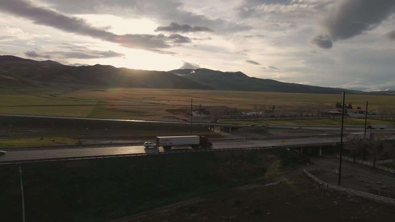 Against a brilliant, golden, partly cloudy sunset, semi trucks cut a striking silhouette, driving south along California's Highway 5, near the Grapevine exit