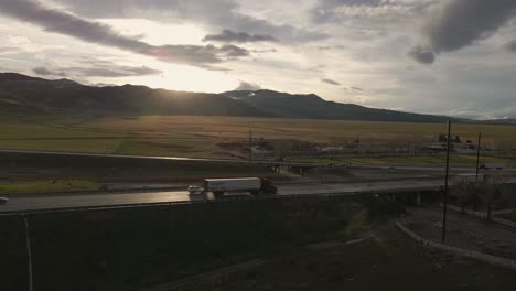 against a brilliant, golden, partly cloudy sunset, semi trucks cut a striking silhouette, driving south along california's highway 5, near the grapevine exit