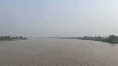 cinematic shot of a muddy river flowing down a bridge joining two lands with industries in bengal, india