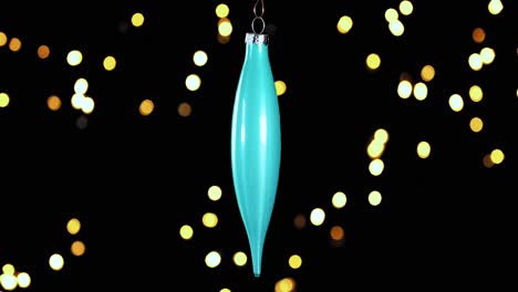 single blue turquoise christmas cone ornament with out of focus lights flickering in the background, close up