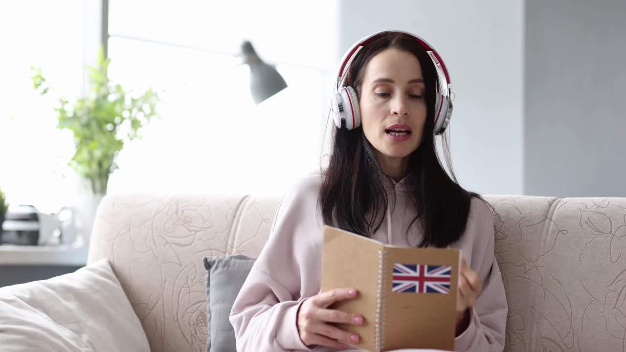A woman studying English with headphones at home, using a notebook with the British flag