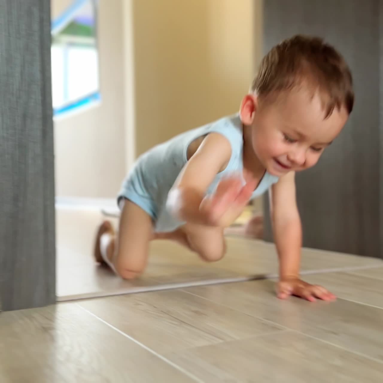 Happy crawling toddler laughs adorably to the camera. Sweet little kid moves by the floor in his house