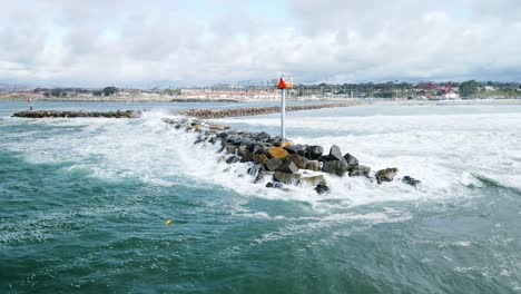 aerial drone landscape above ocean california rock dock with light poles blue dark skyline with some clouds, waves pacific oceanside view