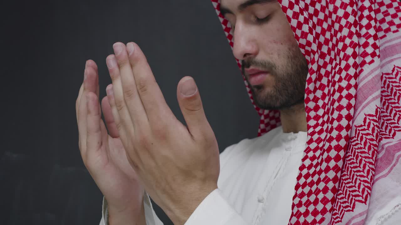 검은색 칠판 앞 에 전통 의 옷 을 입은 남자 가 손 을 넓게 열고 기도 하고 있다