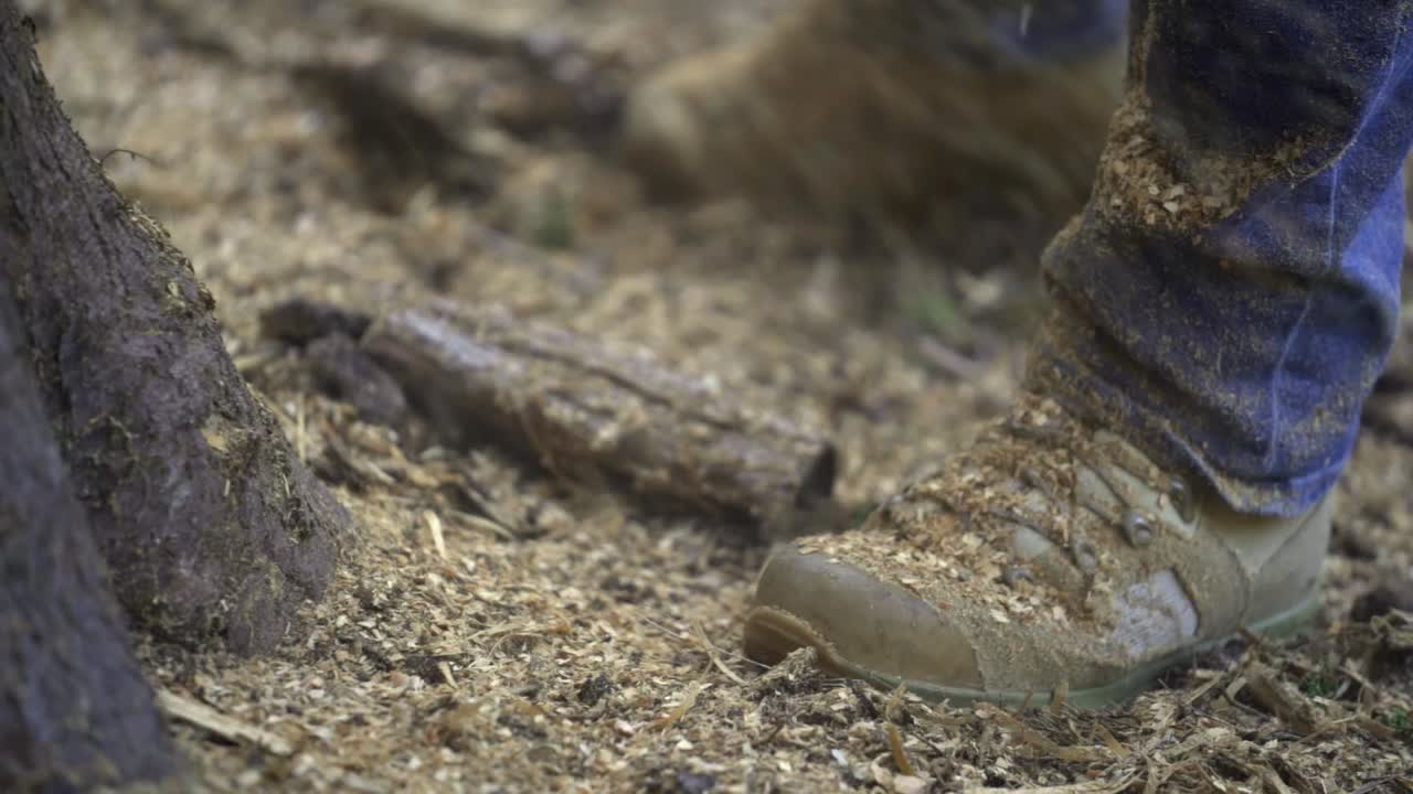 Close up of a loggers shoes with sawdust flying down, guy using chainsaw, slowmo