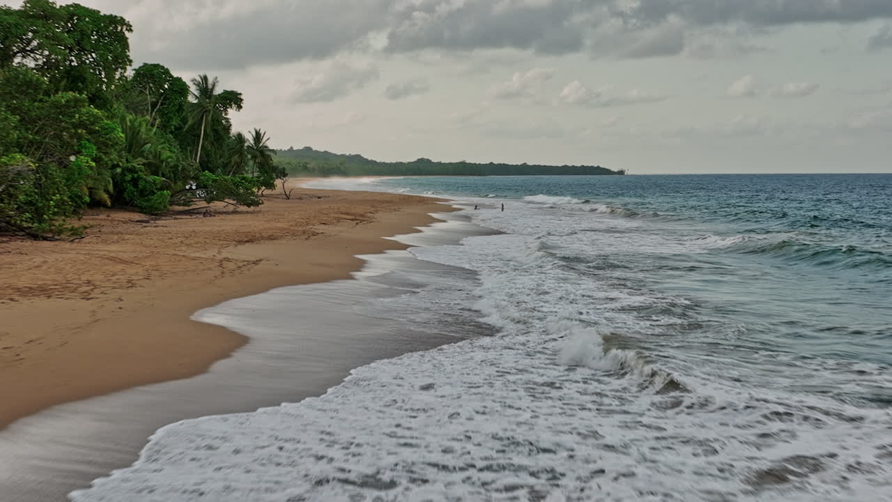 bocas del toro panama aerial v1 cinematic low level flyover along the shore of secluded bluff beach with waves crashing and beachgoers relaxing in the sea water - shot with mavic 3 cine - april 2022