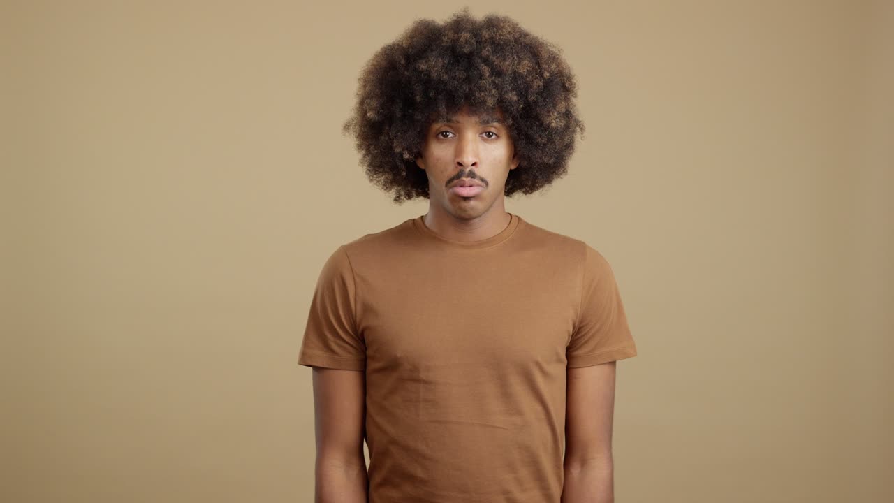 A man with an afro and mustache shows a serious expression, then looks down in shame or sadness.