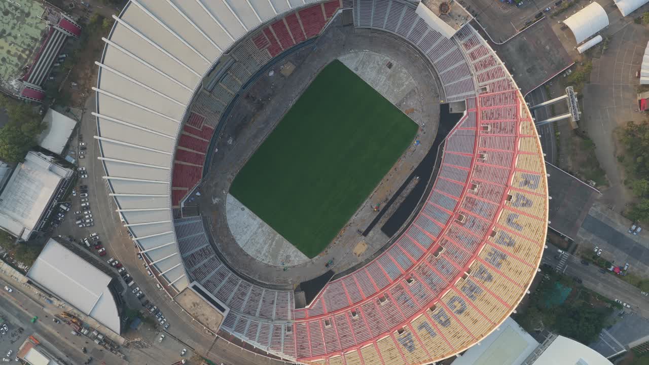 Splendida prospettiva aerea dall'alto di un enorme stadio di calcio vuoto. Il drone ruota lentamente, rivelando l'architettura ovale, le gradinate e il campo in erba verde centrale.