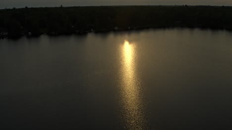 Aerial,-diffused-orange-sunlight-during-sunset-reflecting-on-lake-water