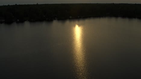 aerial, diffused orange sunlight during sunset reflecting on lake water