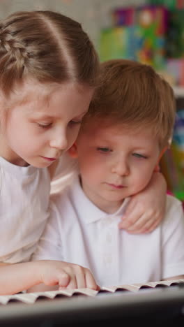 little girl with back braces hugs boy and presses piano keys with brother finger at home lesson. careful sister helps toddler kid remember composition