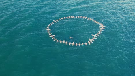 aerial view of dozens of people floating in the sea at samara beach carrying surfboards in a circle formation