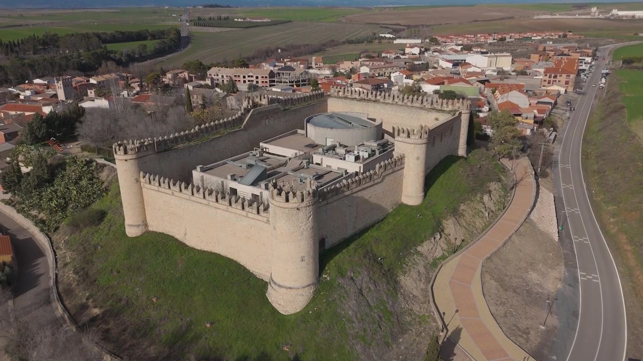 Una ripresa con drone ascendente sul Castello di Maqueda con un movimento della telecamera verso il basso, che rivela la fortezza medievale, le sue strutture interne contemporanee, il villaggio di Maqueda e le montagne distanti.