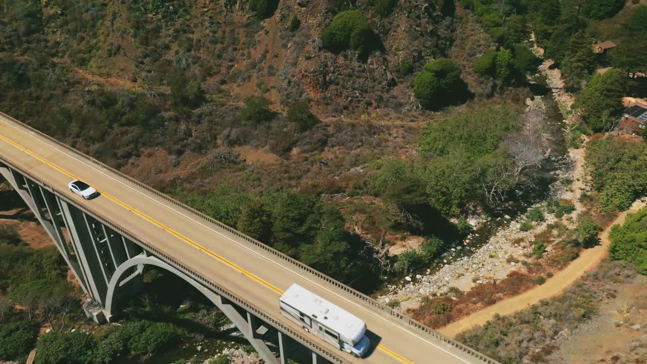 Bridge with cars moving by. Arched bridge in the mountains above the little creek. Aerial view.