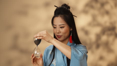 Asian-young-woman-in-blue-kimono-using-hourglass-and-watching-how-sand-pouring-while-counting