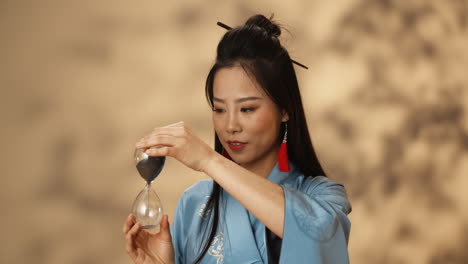 asian young woman in blue kimono using hourglass and watching how sand pouring while counting